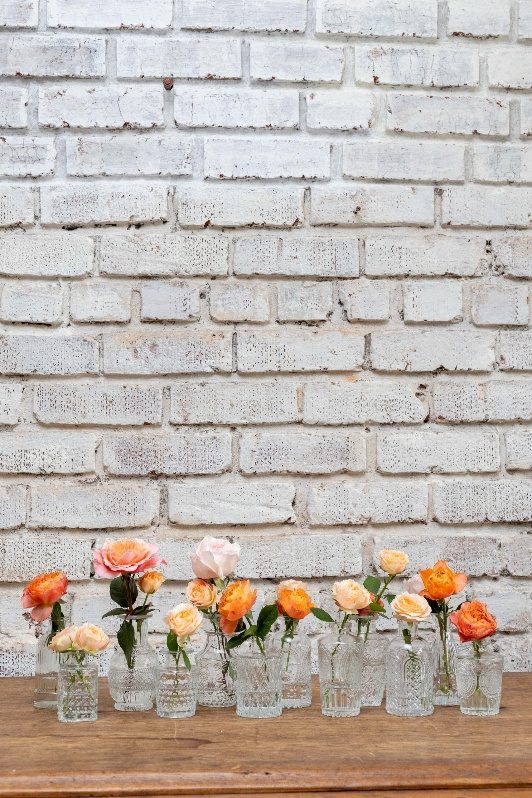 Clear cut-glass bud vases grouped on a wooden table with peach and orange garden roses