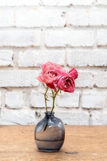 A tinted glass bottle vase holding a small bunch of pink roses